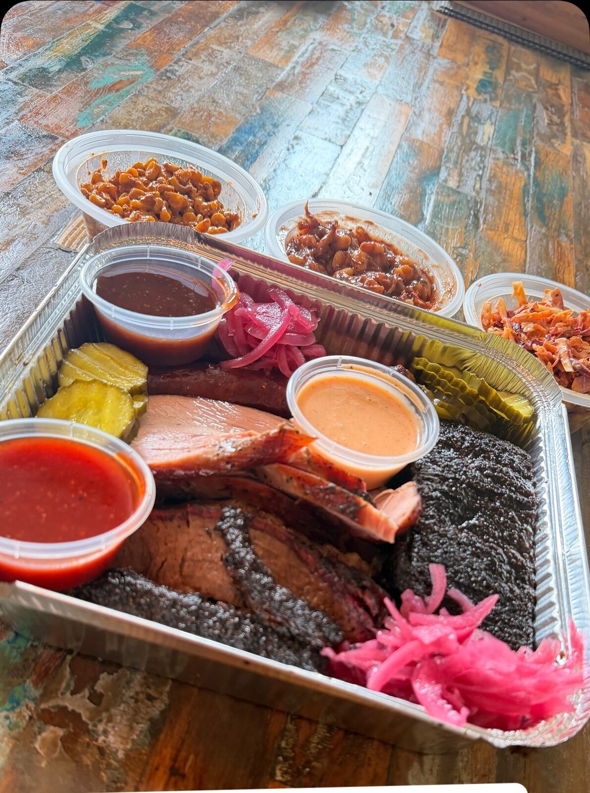 The Pitmaster Selection Tray: brisket, turkey, beef rib and sausage in a foil tray with pit beans, slaw, pickles and three house sauces